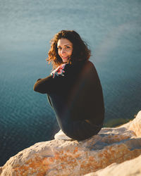 Portrait of woman sitting on rock over sea during sunset