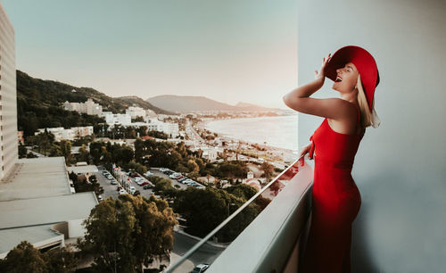 Woman standing on wall in city against sky