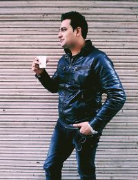 Young man smoking while standing against brick wall