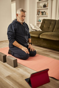 Senior man doing online workout sitting on exercise mat at home