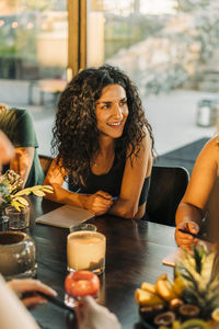 Smiling woman looking away while sitting at dining table in retreat center