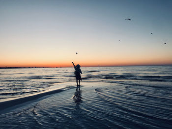 Silhouette man on beach against sky during sunset