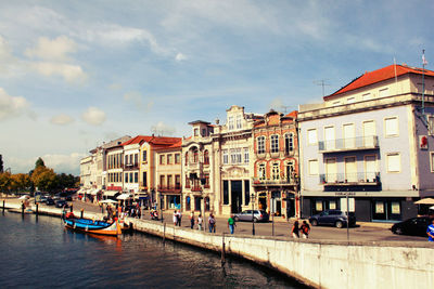 Boat in canal by buildings against cloudy sky in city on sunny day