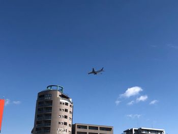 Low angle view of airplane in flight building against blue sky