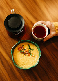 Yellow healthy pumpkin vegetarian porridge in a plate, a pot of tea and a mug on a wooden table