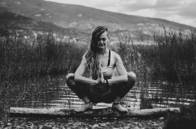 Full length of young woman meditation by pond outdoors