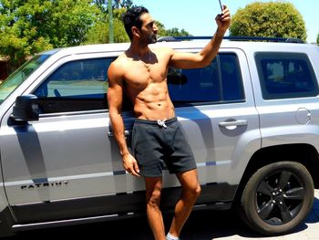 Shirtless man taking selfie against car