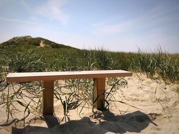 Bench on beach against sky