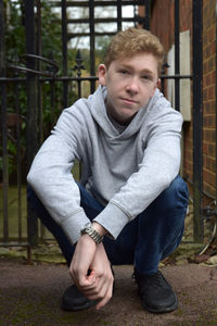 Portrait of teenage boy crouching against gate