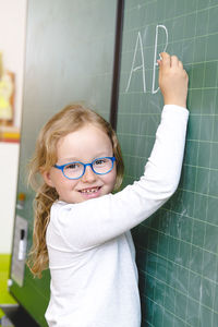 Portrait of smiling girl writing alphabets on blackboard