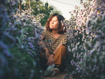 Portrait of young woman sitting on purple flowering plants