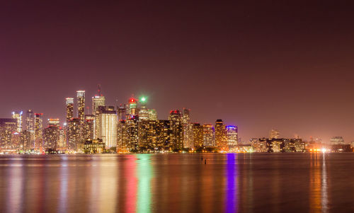 Illuminated cityscape by river against sky