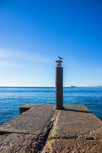 Lighthouse by sea against blue sky