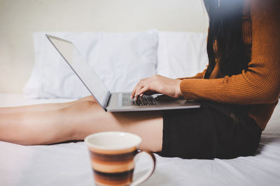 Midsection of woman using mobile phone while sitting on bed