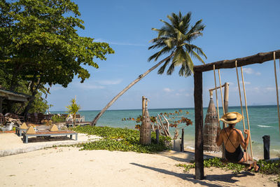 Rear view of woman sitting on swing at beach