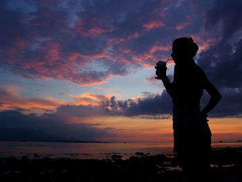 Silhouette woman photographing sea at sunset