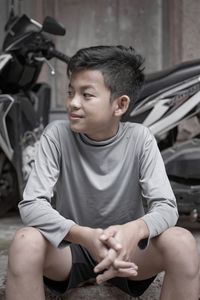 Smiling boy sitting against motor scooter