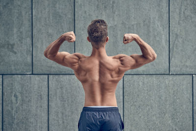 Shirtless man flexing muscles against wall