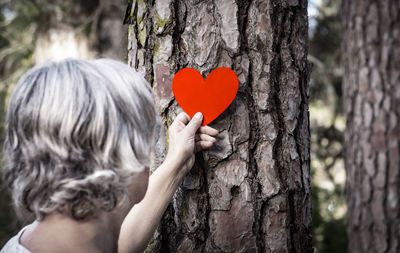 Close-up of woman holding heart shape on tree trunk