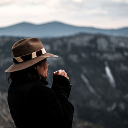 Woman in hat having coffee against mountains during winter