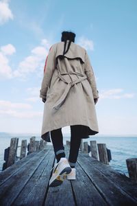 Rear view of woman standing on pier by sea against sky