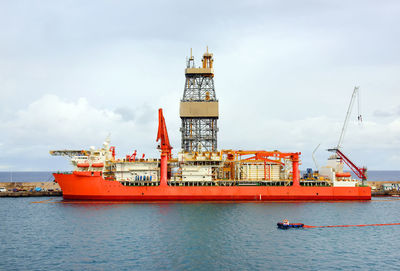 Ship by oil rig at sea against sky