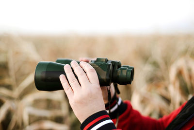 Cropped image of hand holding camera against sky