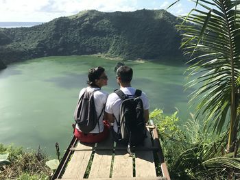 Rear view of men sitting on riverbank against sky