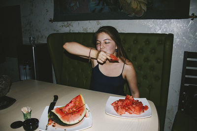 Woman eating watermelon while sitting at table