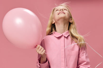 Girl looking up holding balloon against pink background