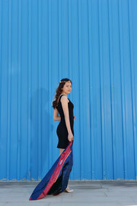 Side view of woman standing against blue wall