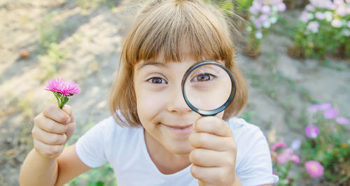 Portrait of smiling girl holding flower looking through magnifying glass