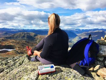 Rear view of woman sitting on rock against mountains and sky