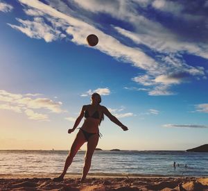 Woman in bikini playing with ball at beach against blue sky