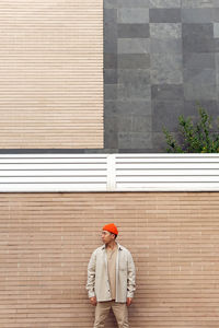 Calm serious stylish male in casual outfit standing against masonry wall looking way