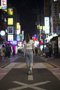 Rear view of woman walking on illuminated street at night