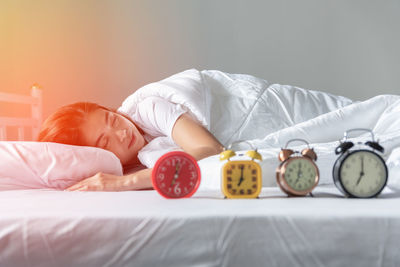 Midsection of woman with alarm clock on bed at home