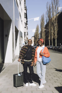 Full length portrait of father and daughter standing on footpath during sunny day