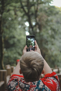 Rear view of man photographing from mobile phone at forest