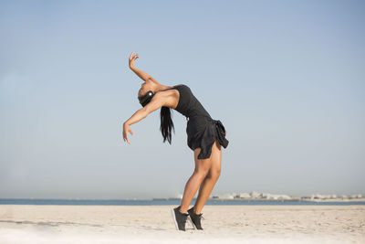 Young woman dancing at beach against clear sky