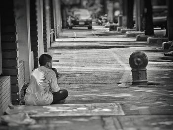 Rear view of homeless boy sitting on sidewalk