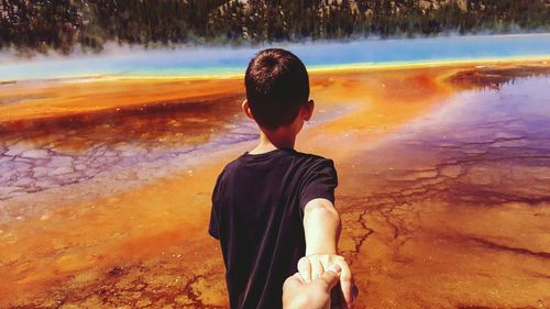 Cropped hand holding boy by geyser at yellowstone national park