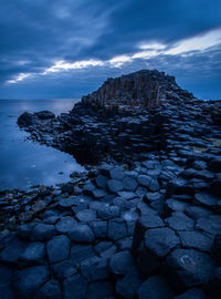 Scenic view of rock formations at beach against cloudy sky at dusk