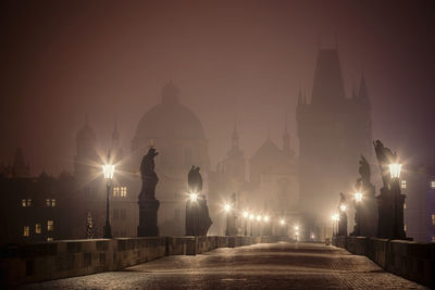 Illuminated bridge against buildings at night