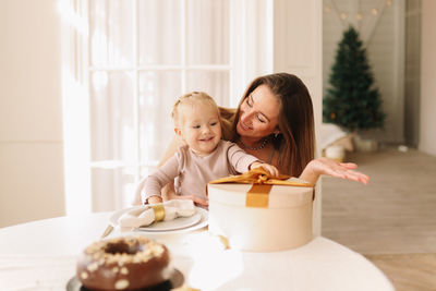 Happy mom and child are sitting at the dining table eating a christmas cake on holiday at home