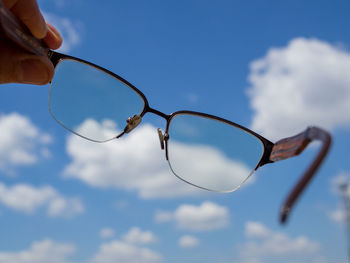 Close-up of hand holding sunglasses against sky