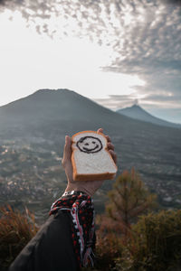 Cropped hand of holding bread against mountains