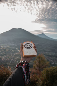 Midsection of person holding camera against mountains