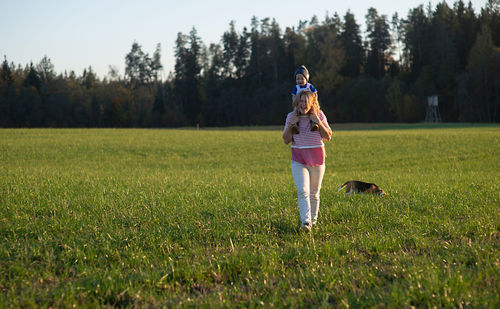 Happy mother carrying son on shoulders while walking on grassy field in park