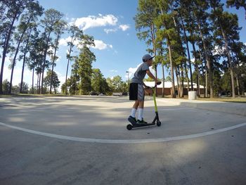 Side view of boy riding push scooter on field against sky